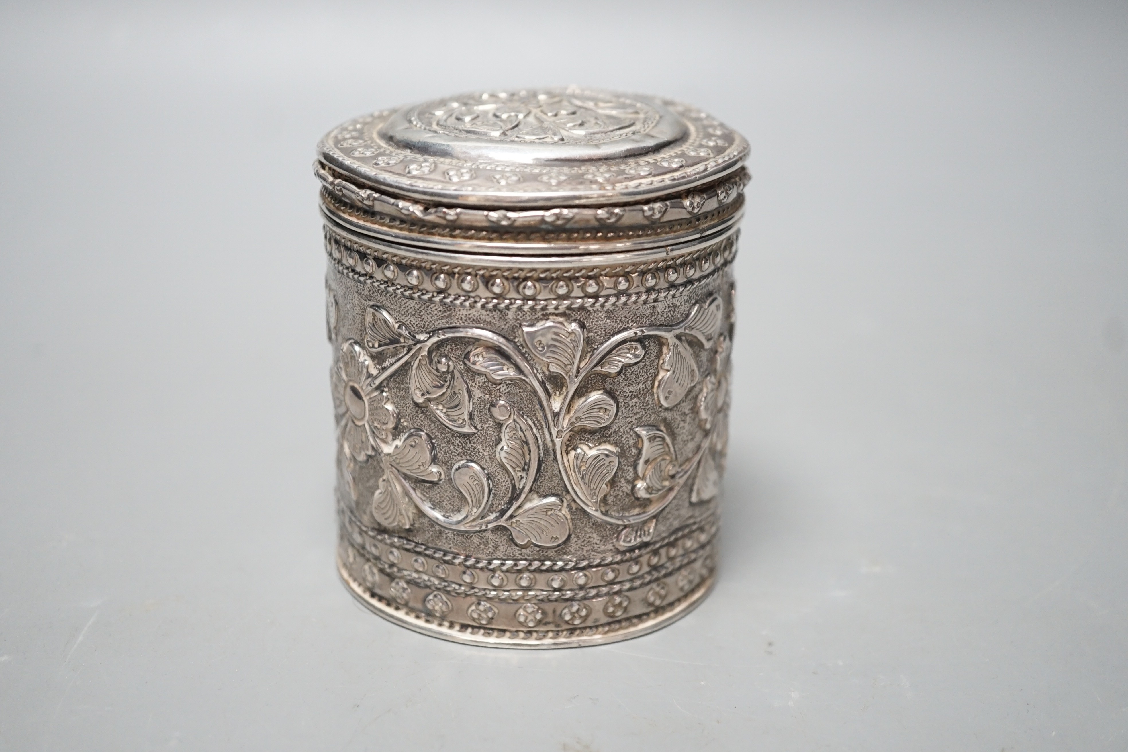 An Indian embossed white metal cigar case, 12.2cm and a similar canister and cover.